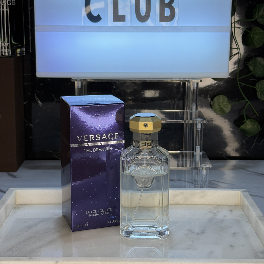 Versace The Dreamer — frasco original sobre superficie negra reflectante con fondo carbón, Parfaria Club