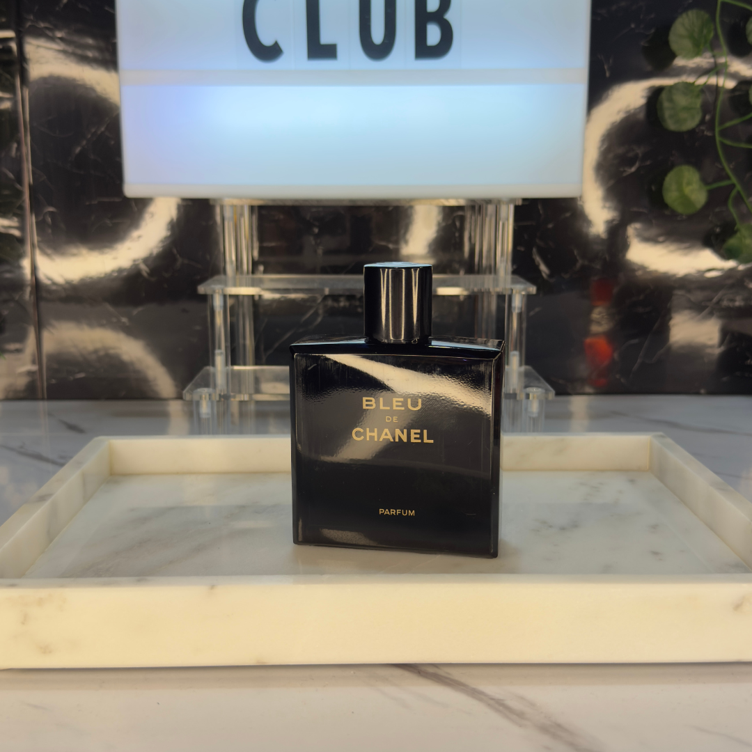 Bleu de Chanel Parfum — frasco original sobre superficie negra reflectante con fondo carbón, Parfaria Club