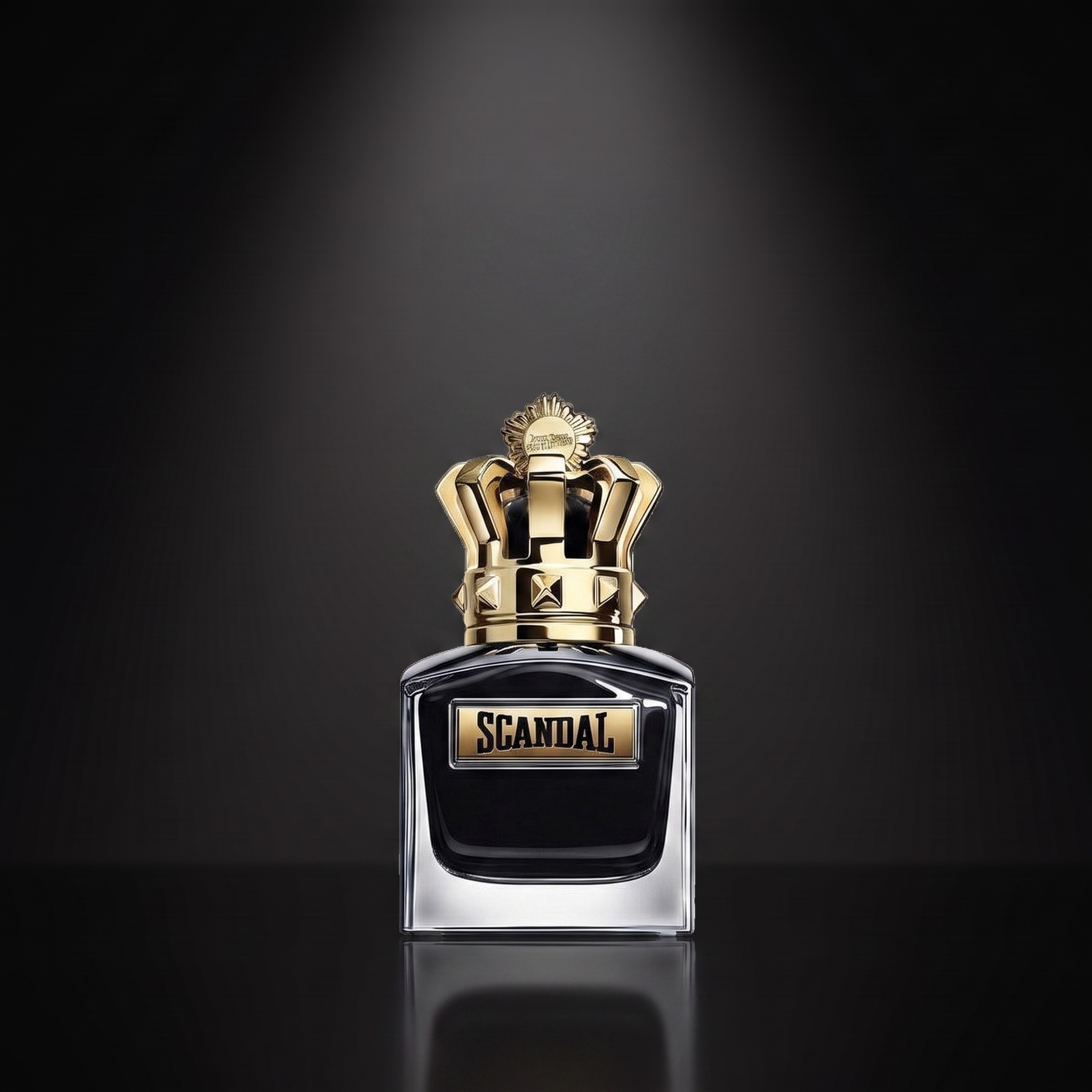 JPG Scandal Le Parfum — frasco sobre superficie negra reflectante con fondo carbón